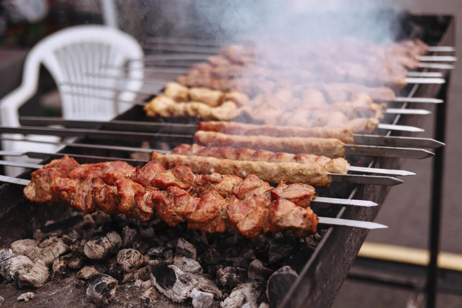 Juicy skewered meat grilling on open flame barbecue outdoors, perfect for dinner party.