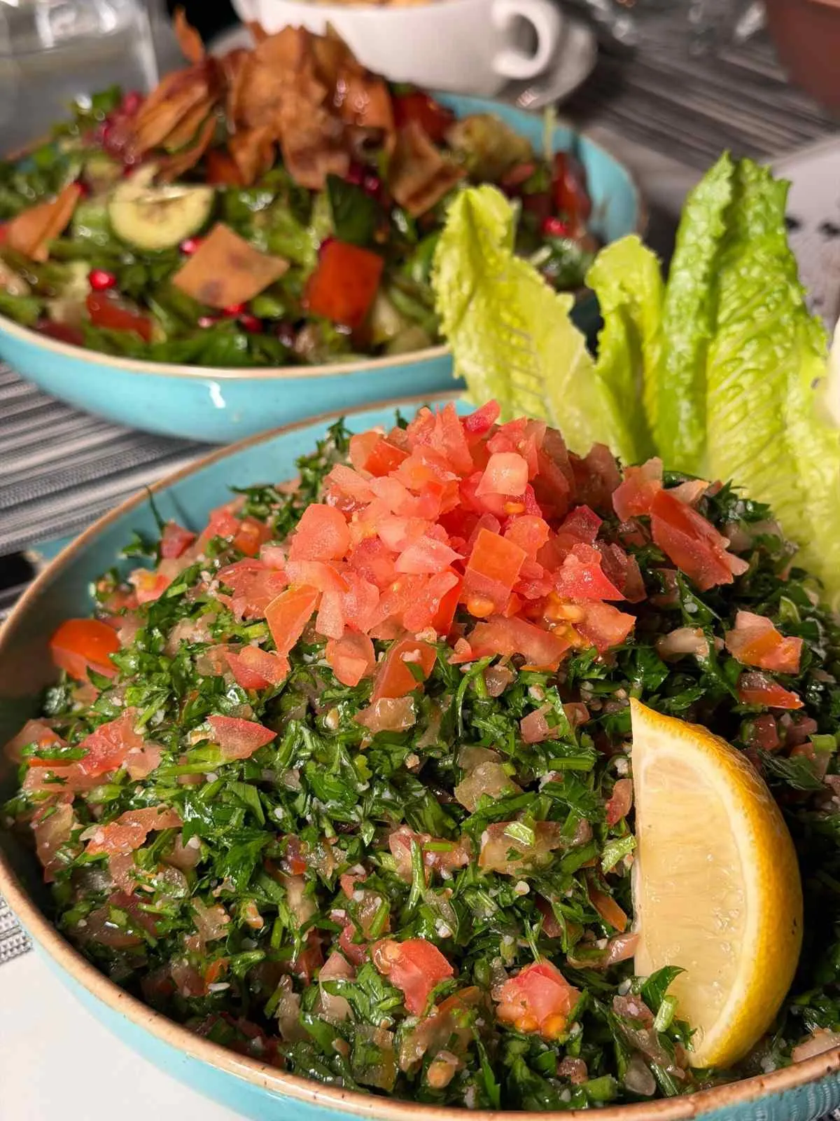 Vibrant tabbouleh and fattoush salad with fresh vegetables and a lemon wedge.